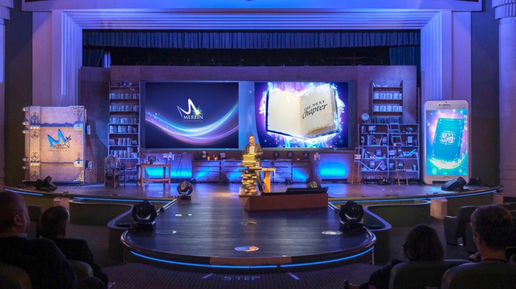 Event production for conferences and events showing an example of corporate stage deisgn with a speaker and large prop books in front of an LED screen.