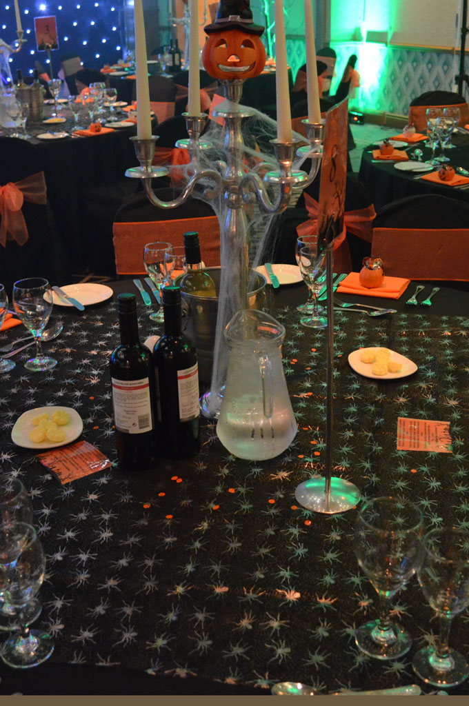 An example of corporate event production with a halloween themed decorated round table with drinks, spider tablecloth, more tables behind.