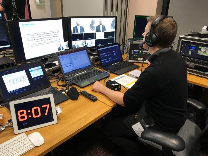 Seated man in front of monitors wearing headphones involved in audio-visual production as offered by an event production company.