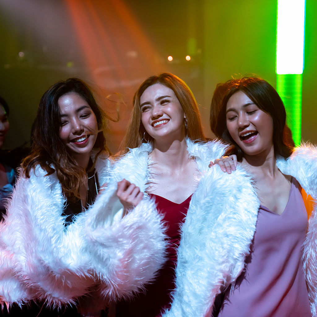An example of corporate event production with three young women attendees in costume singing karaoke under coloured lights, at a team building event.