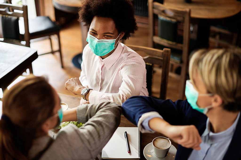 Three colleagues wearing covid masks touching elbows in a post-pandemic conference specialists type working environment.